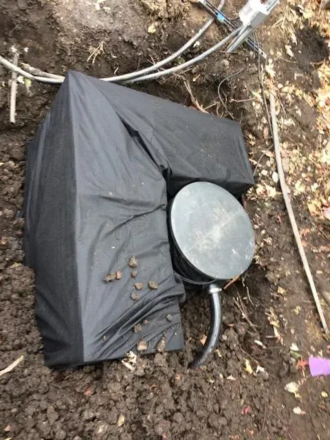 A black tarp is covering a metal object in the dirt.