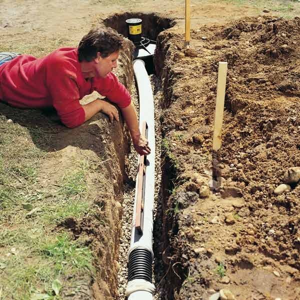 A man in a red shirt is laying in the dirt next to a pipe