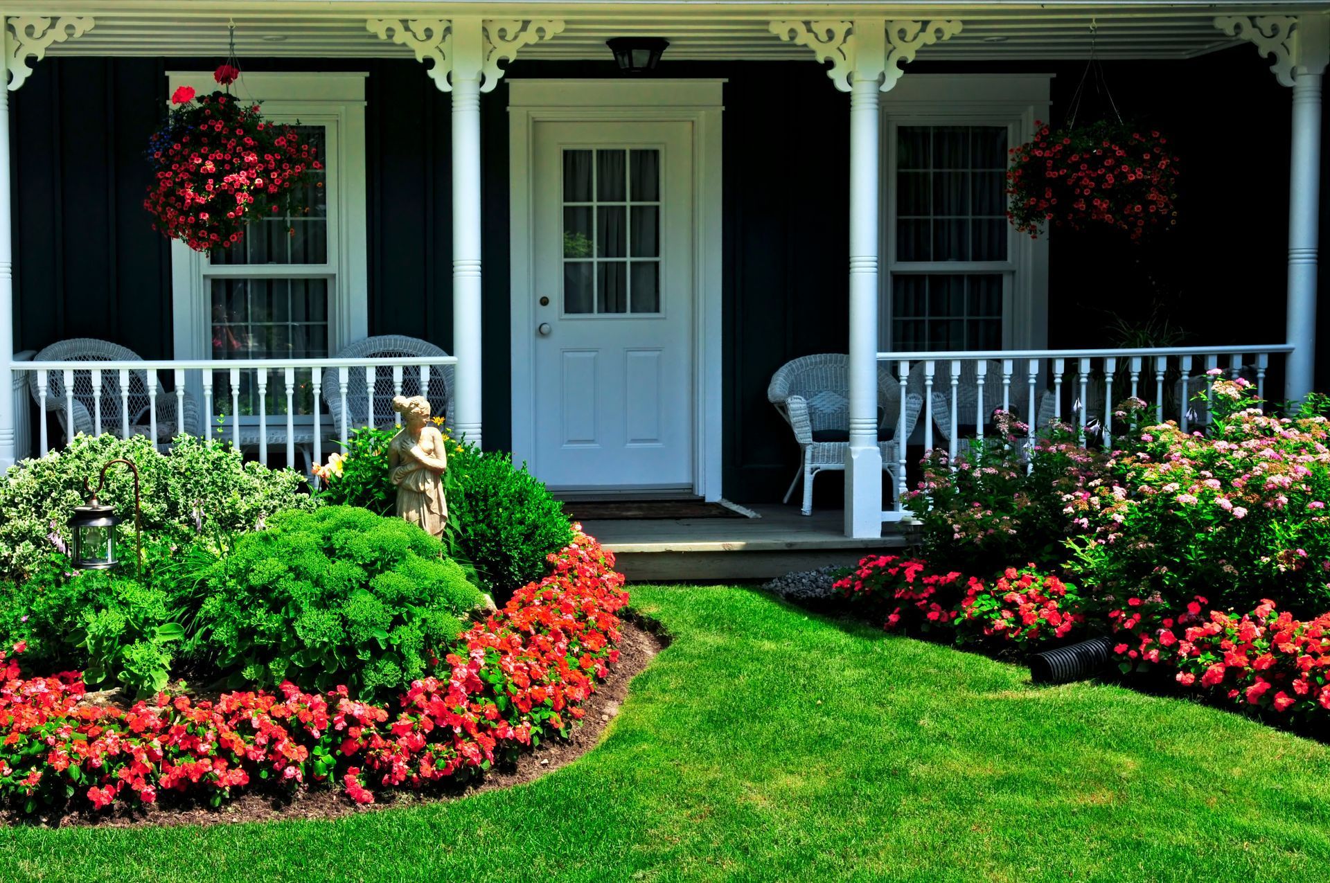 A black house with a white porch and flowers in front of it.