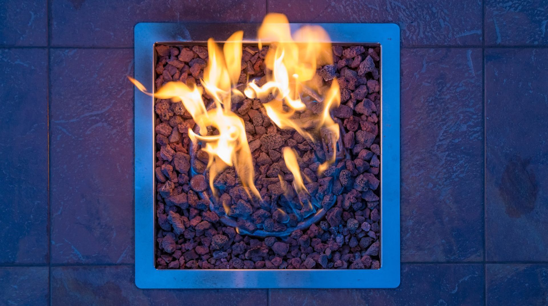 A fire pit with flames coming out of it is on a tiled floor.