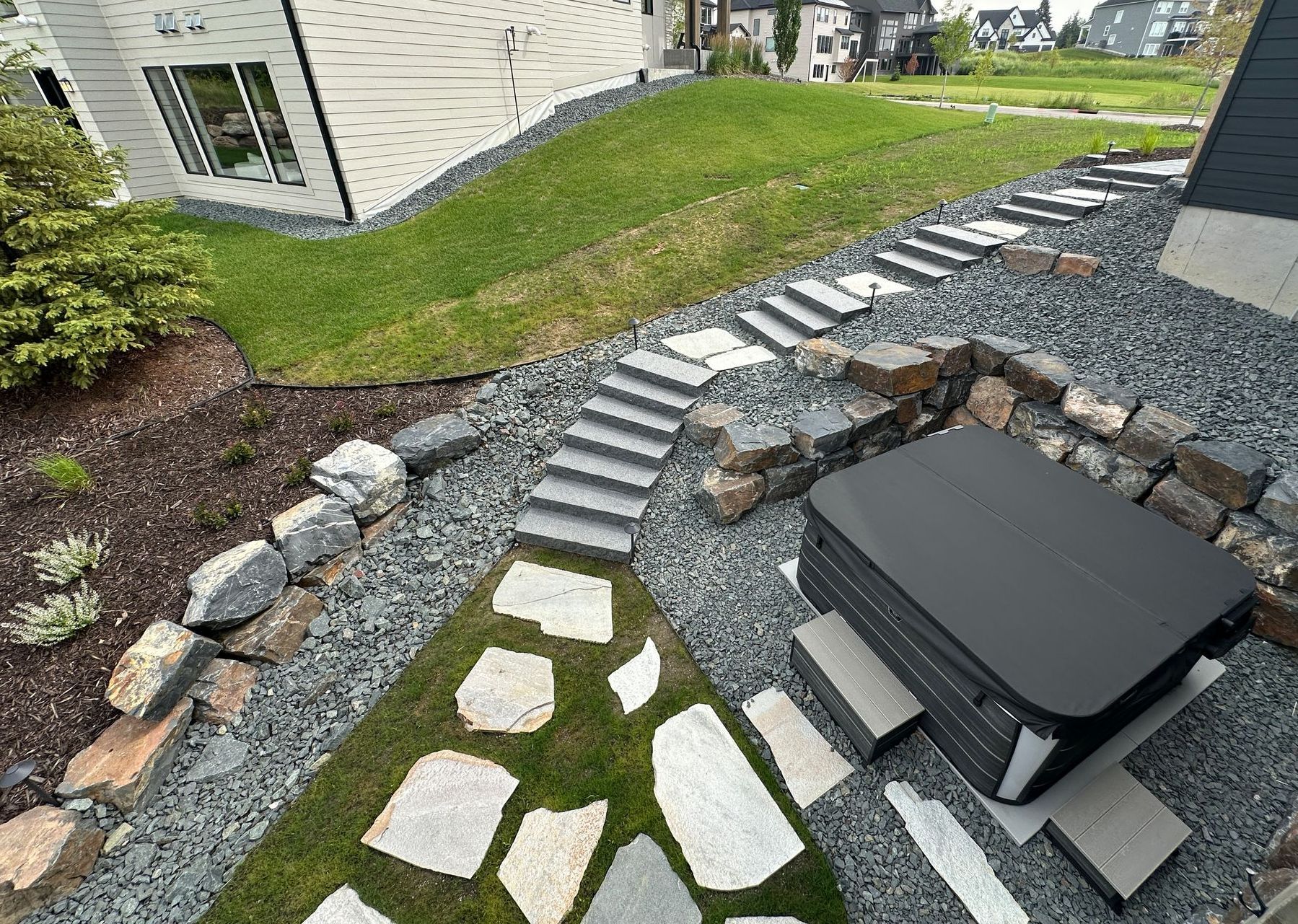 Hot tub area carved into hillside with large gray boulder wall stone steps large flagstone steppers set into lawn 3/4 trap rock KG Landscape MN