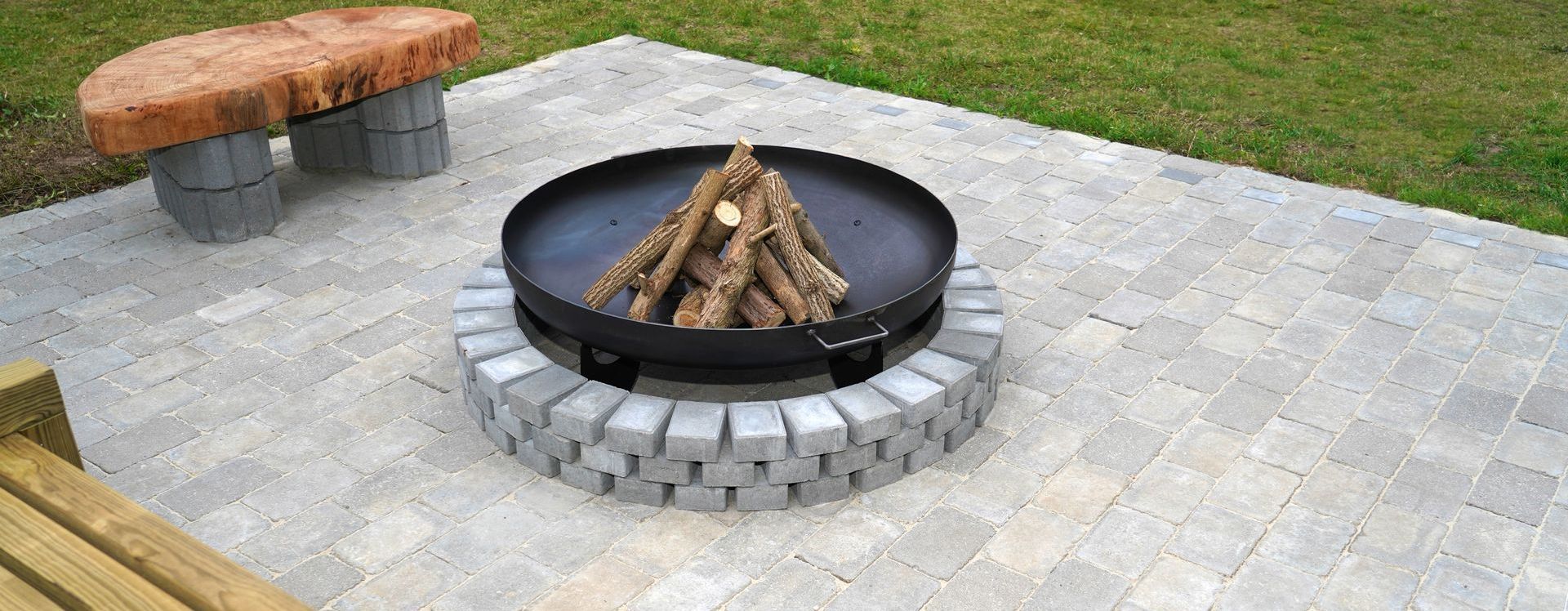 A fire pit is sitting on a patio next to a bench.