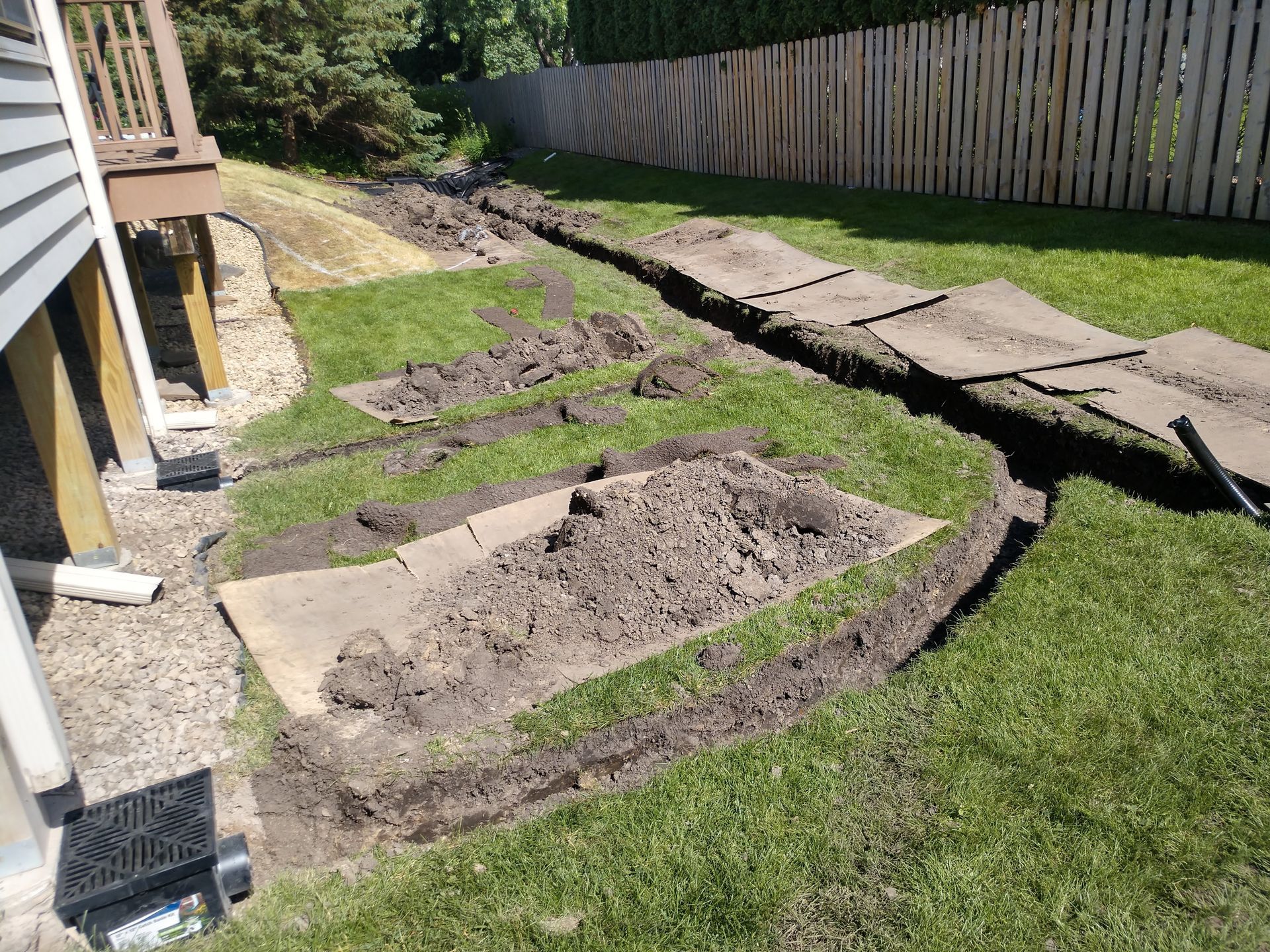 New landscape drainage system being installed with catch basin below down spouts and French drain 