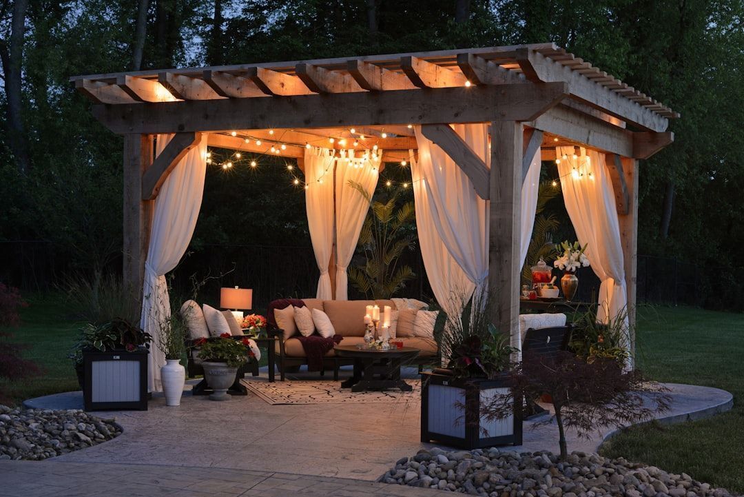 A gazebo with a couch and curtains is lit up at night.