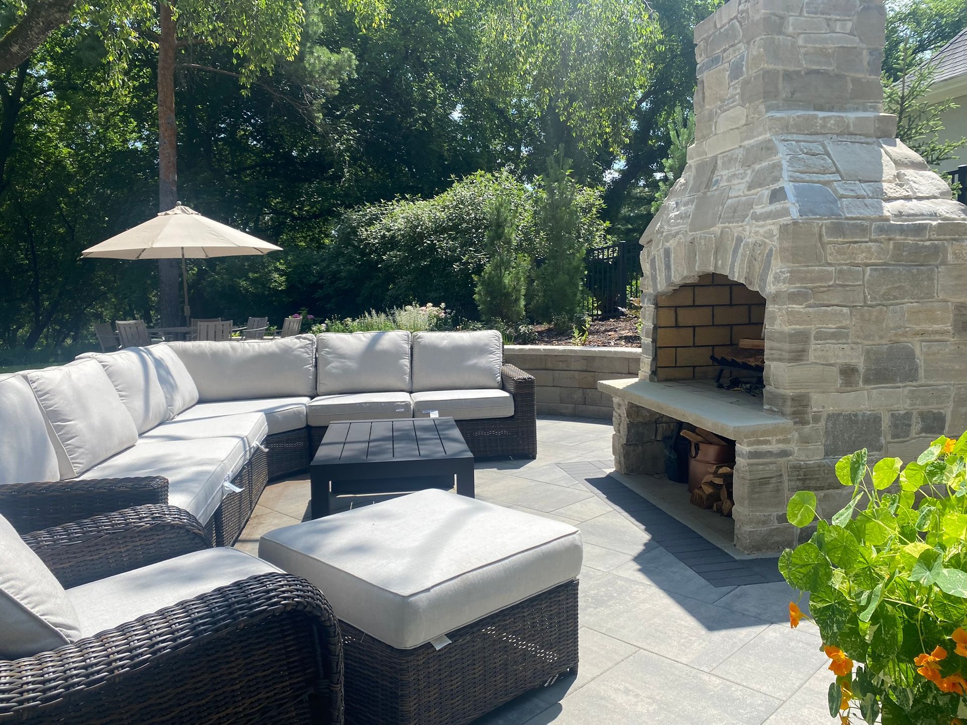 Patio design and installation Minnetonka MN KG Landscape fire feature gray pavers surrounded by a retaining wall fireplace with outdoor wicker furniture couch and chairs  