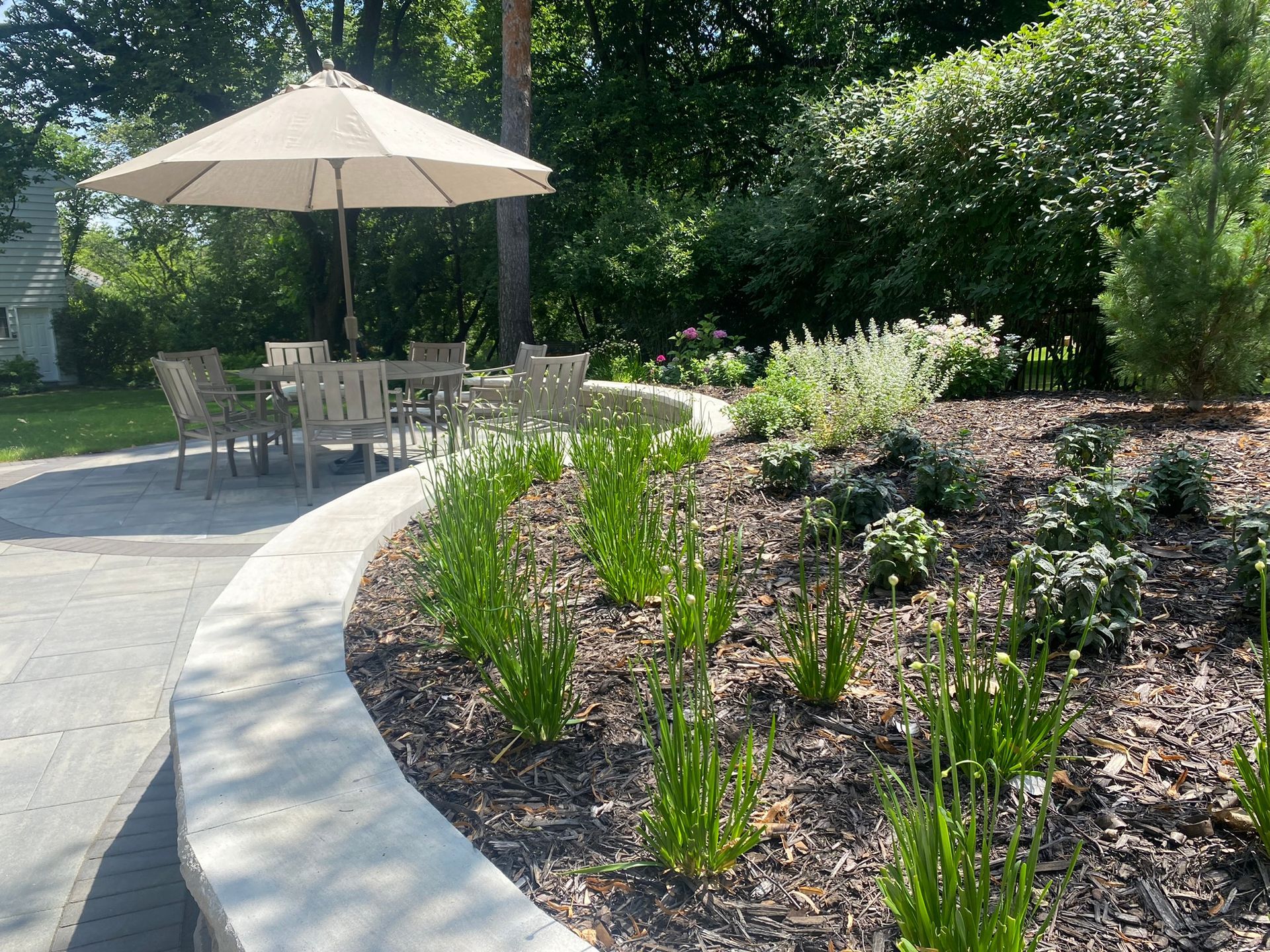 Paver stone backyard patio design inspiration ideas  Minnetonka Minnesota KGLandscape.com Curvilinear shape sitting wall capstone around patio with colorful perennials light gray natural stone fireplace furniture 