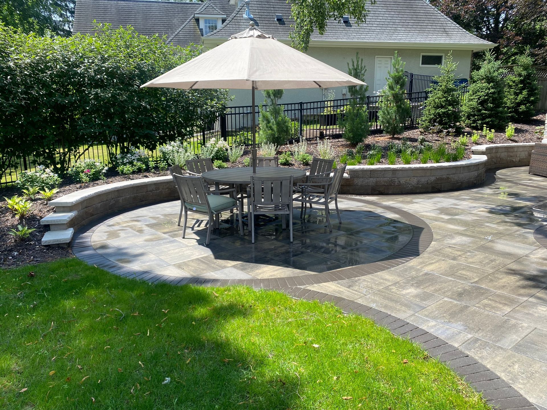 Paver patio design inspiration ideas dining table and chairs with umbrella within circular paver inlay Minnetonka Minnesota KGLandscape.com sitting wall and Indiana limestone capstone around patio colorful perennials