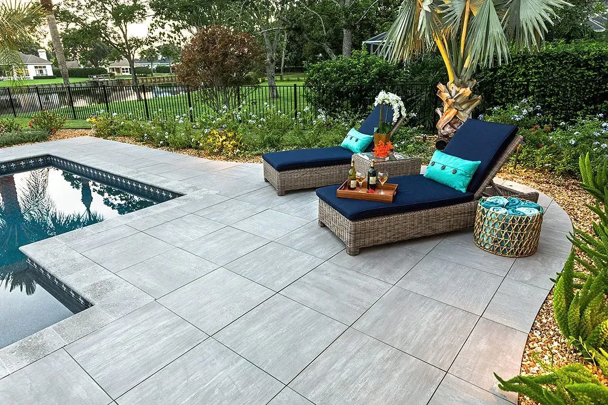 Two lounge chairs are sitting on a patio next to a pool.