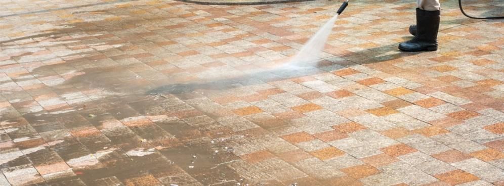 A person is using a high pressure washer to clean a brick floor.