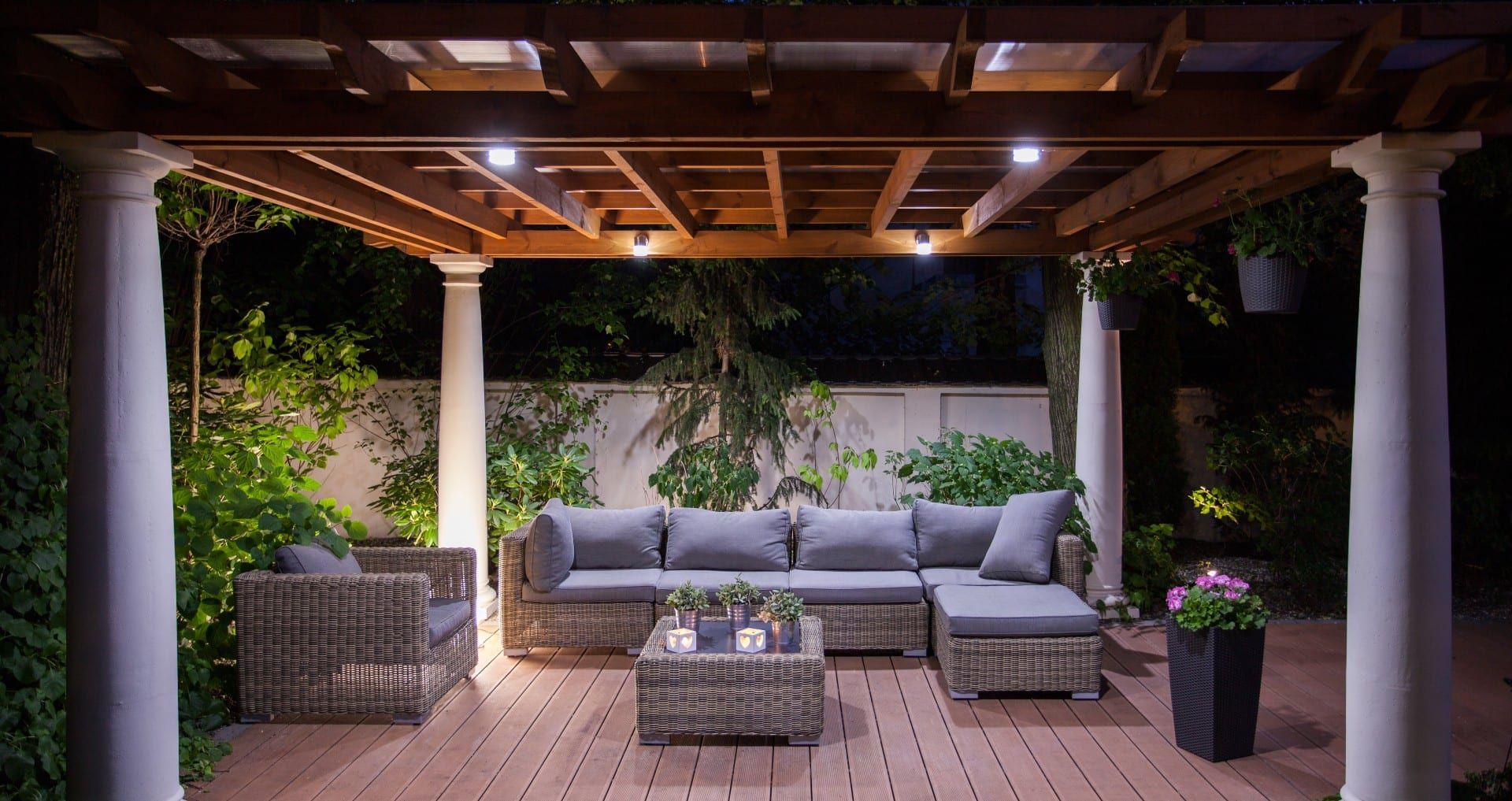 A patio with a couch and chairs under a pergola at night.