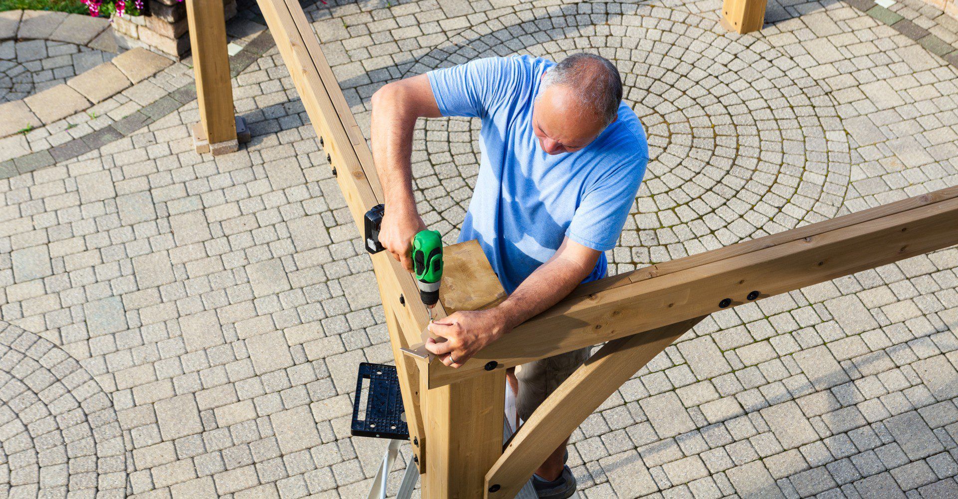 A man is working on a wooden structure on a patio.