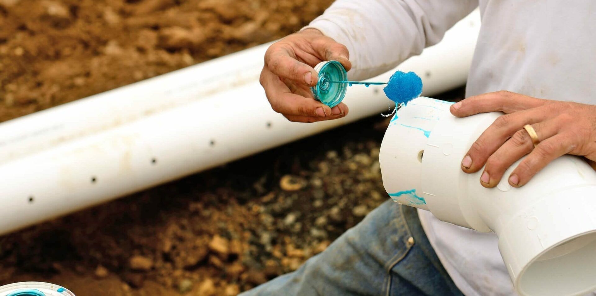 A man is cutting a piece of plastic pipe with a pair of scissors.