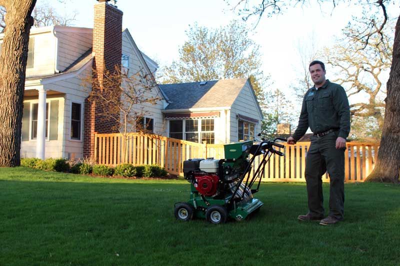 A man standing next to a green lawn mower in front of a house