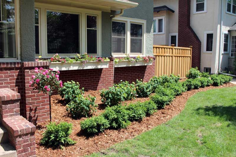 A brick house with a wooden fence and bushes in front of it