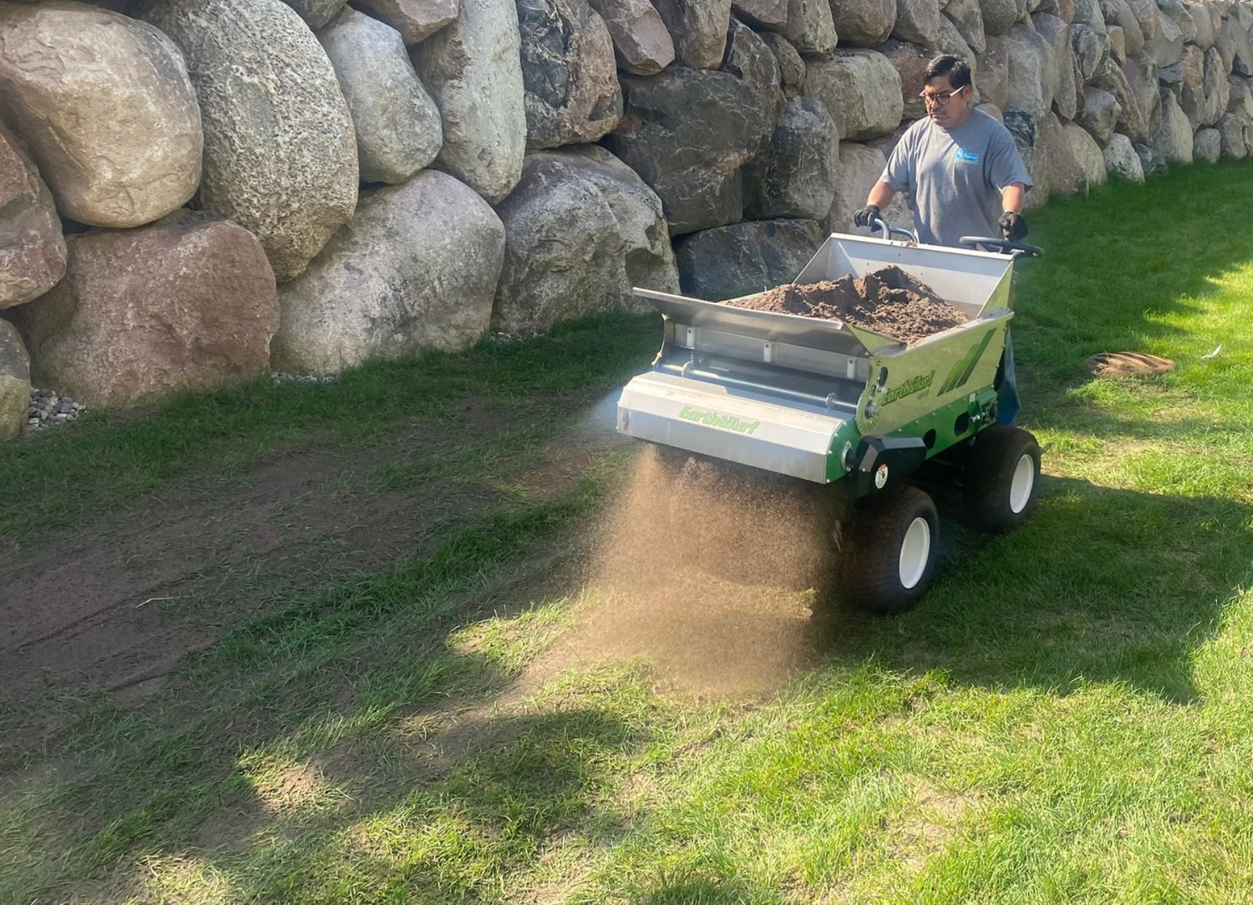 foreman topdressing a lawn with boulder wall in the background