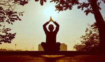 A silhouette of a person sitting in a lotus position with the sun behind them.