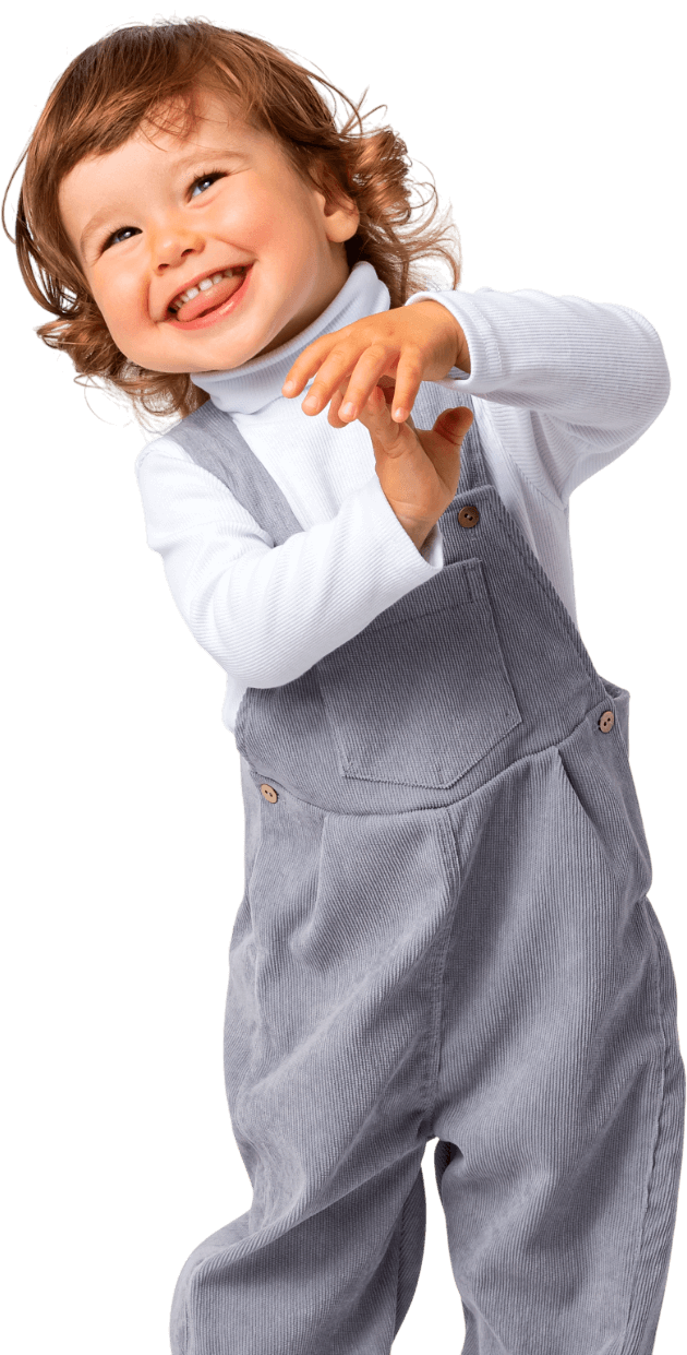 A little girl wearing overalls and a white turtleneck is smiling.