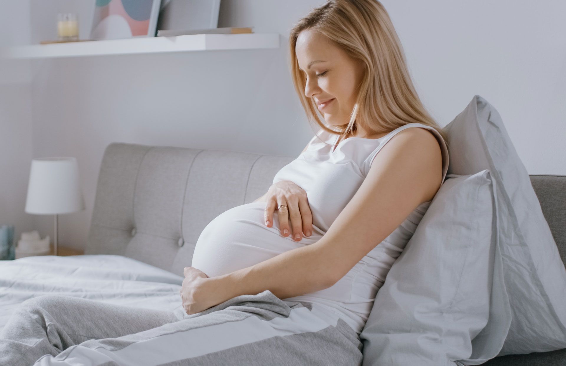 A pregnant woman is sitting on a bed holding her belly.