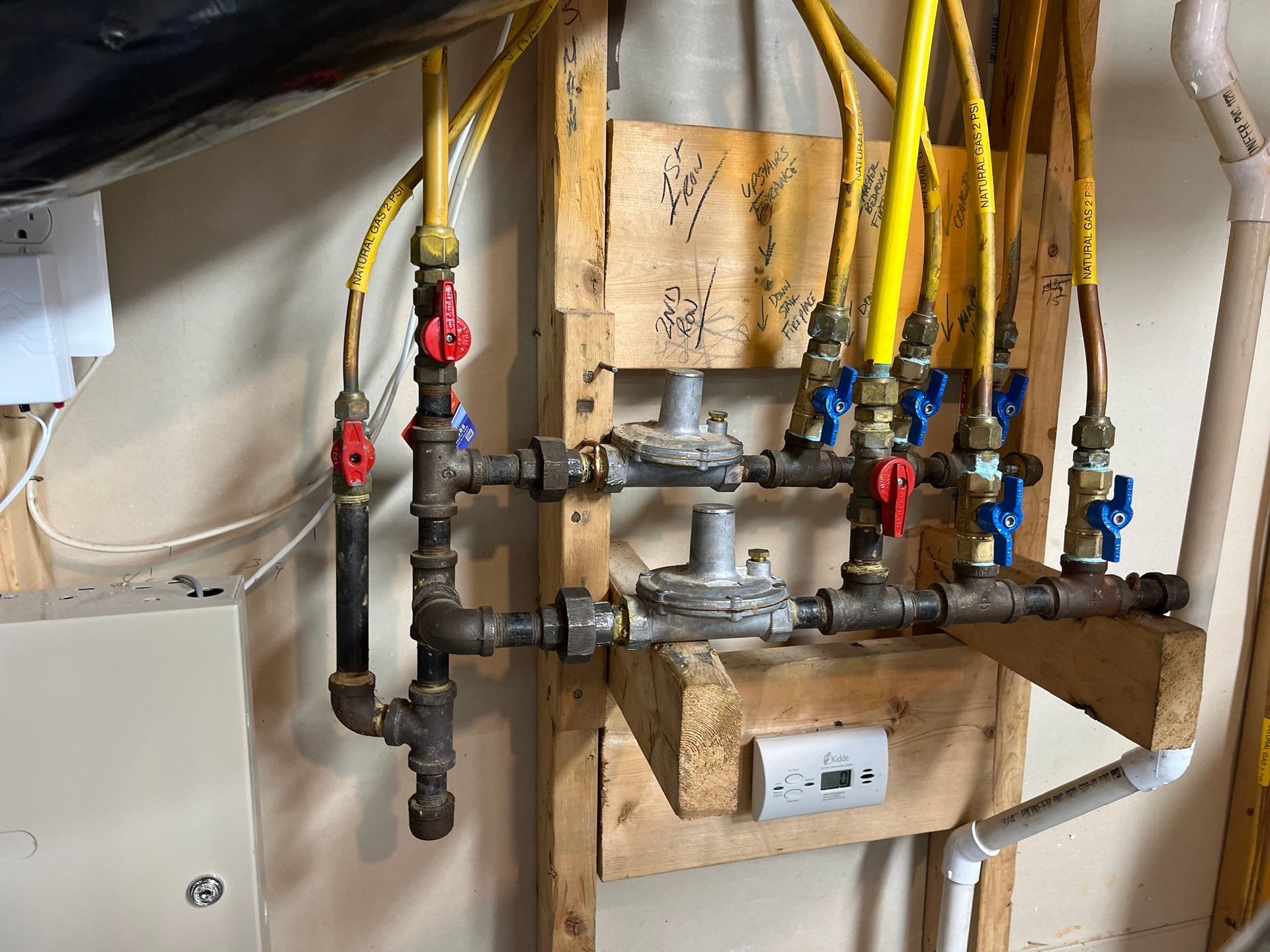 Gas line manifold with yellow and black pipes, red and blue valves, mounted on wood.