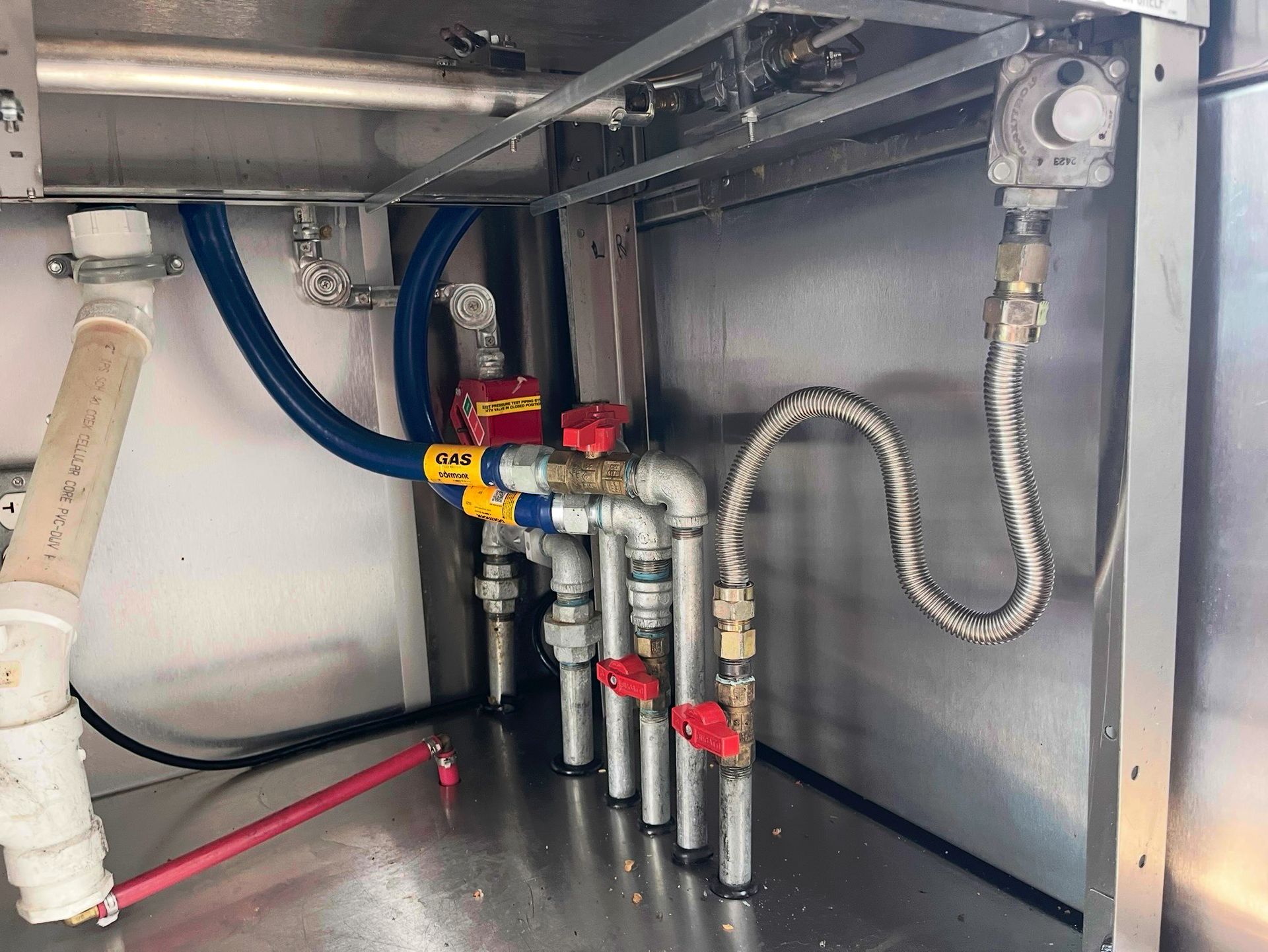 Piping and valves inside a metal compartment. Blue and silver pipes with red and yellow valves.