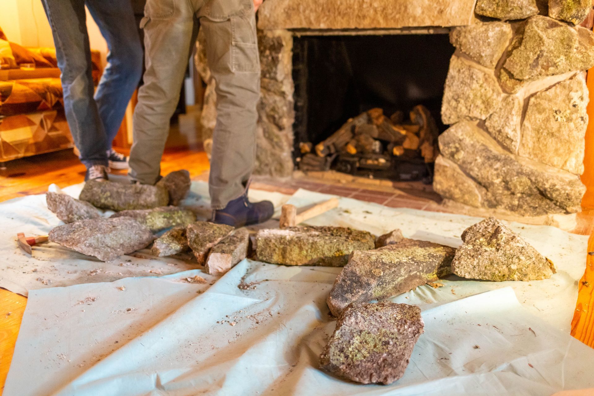 Person in blue shirt and khaki pants working on a fireplace, on a wood floor.