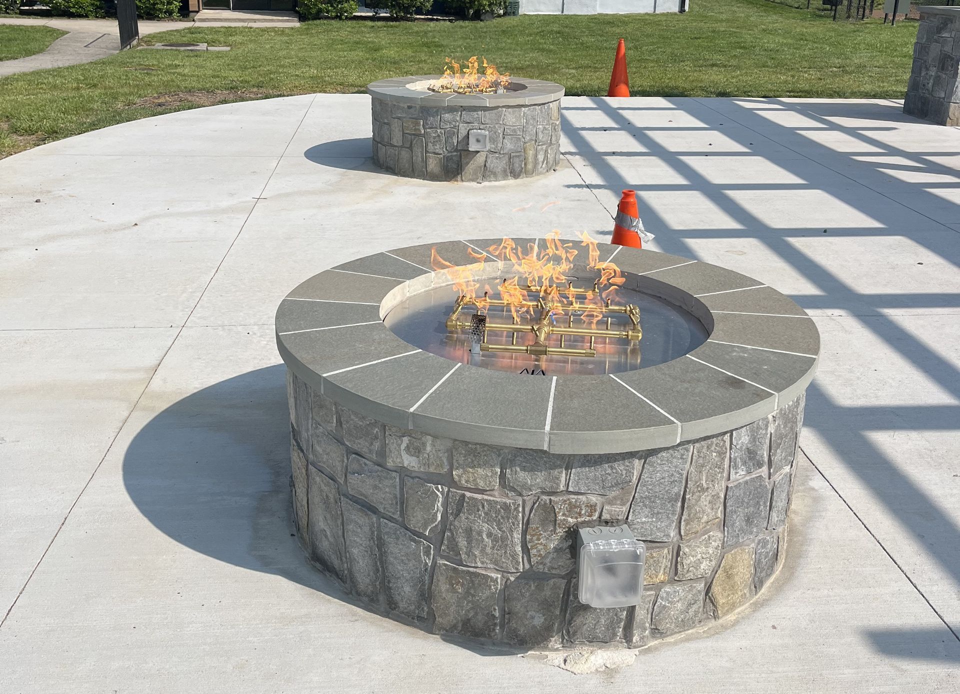 Two Lit Stone Fire Pits On A Concrete Patio Orange Cones In The Background — Falls Church, VA — Nova Gas