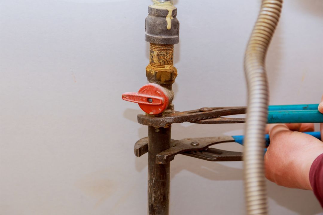 Person using pliers on a corroded gas valve attached to a white wall.