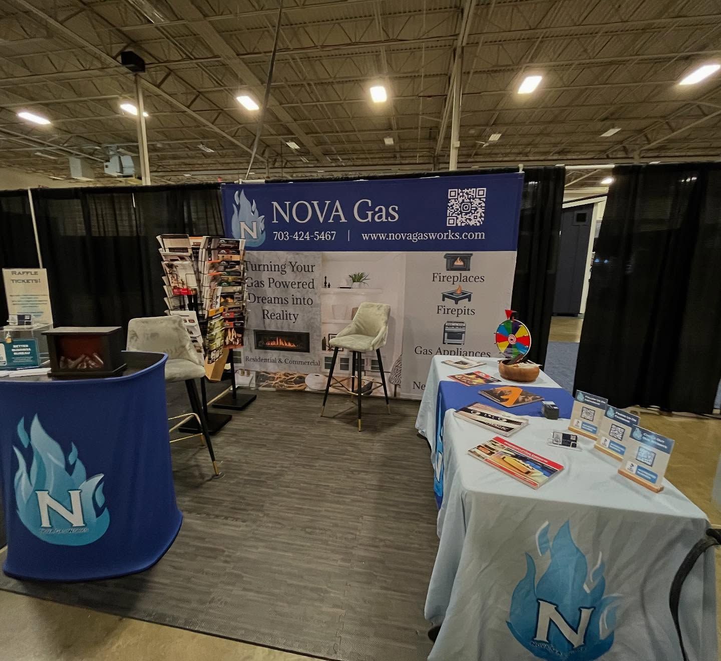A trade show booth for Nova Gas featuring branded blue tables, a fireplace display, and a backdrop with company branding.