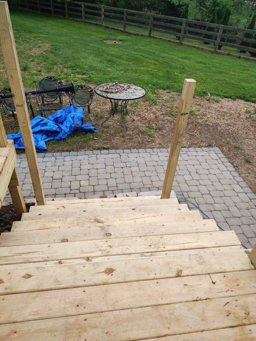 A wooden deck with stairs leading up to a brick patio.