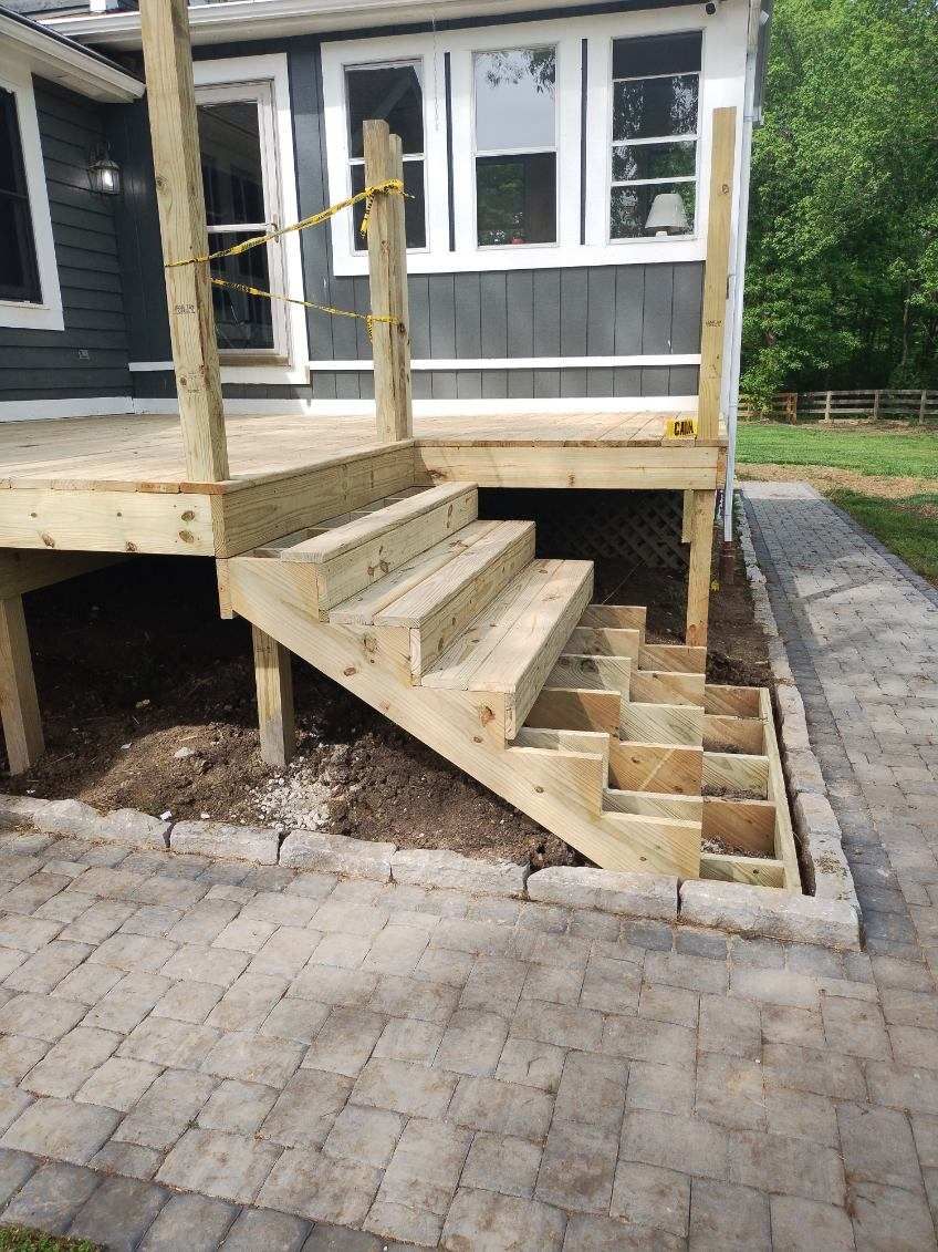 A wooden deck with stairs leading up to it is being built in front of a house.