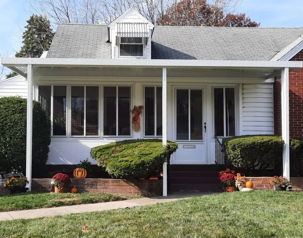A white house with a porch and pumpkins in front of it