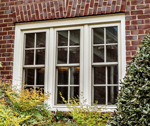 A brick building with a white window and a bush in front of it