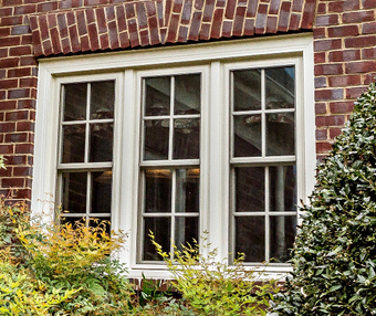 A brick building with a white window and a bush in front of it