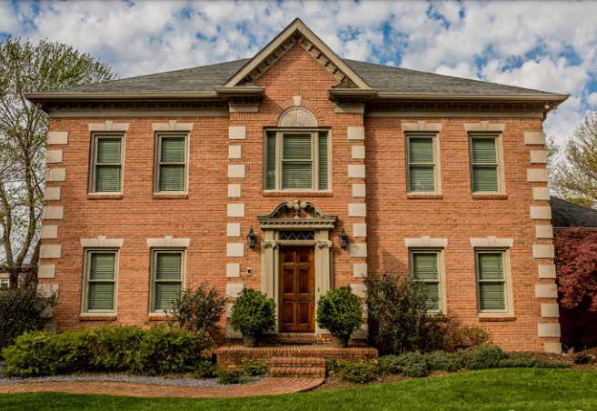 A large brick house with green windows and a gray roof