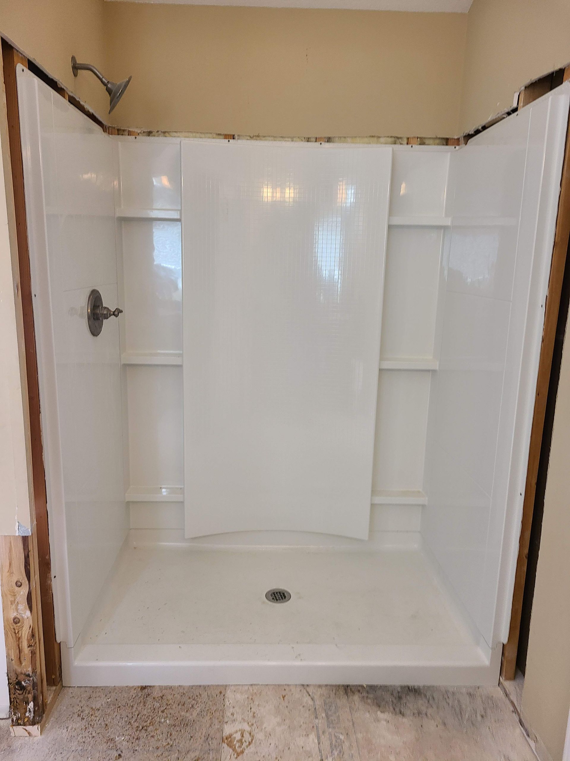 White shower stall with shelves and a faucet, being installed in a room.