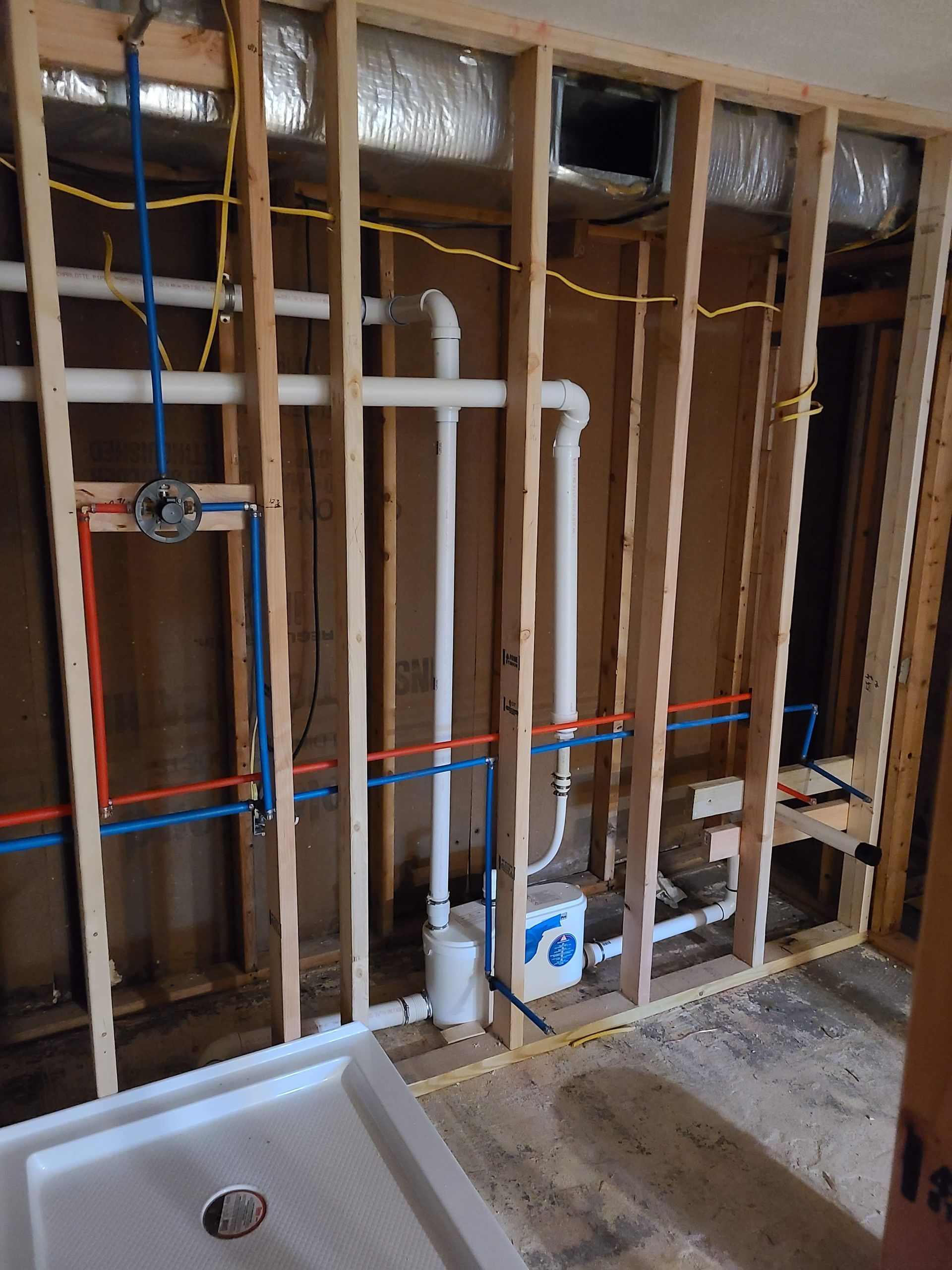 Bathroom under construction with exposed wood framing, plumbing, and shower base.