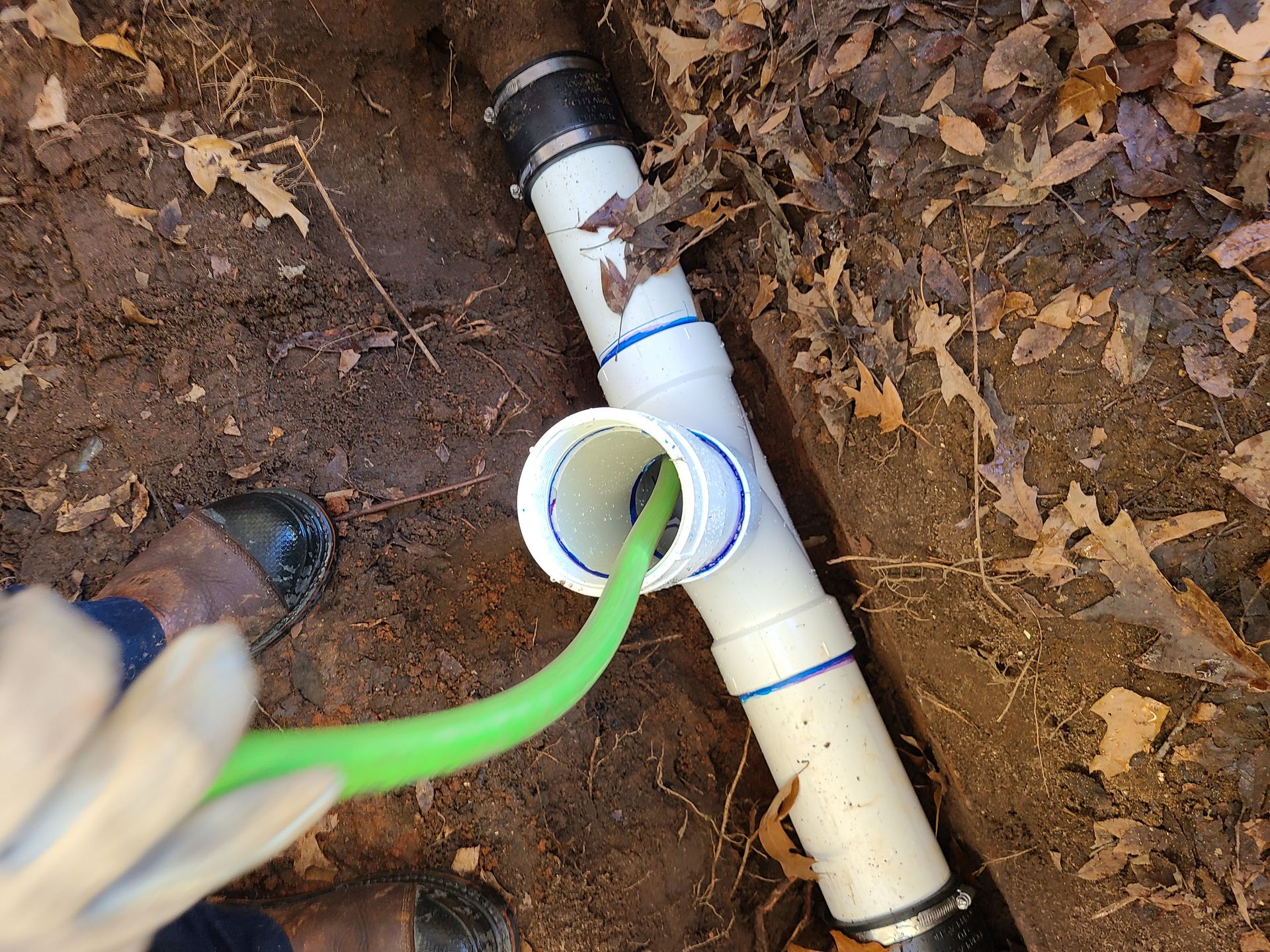 PVC pipe with a green hose inserted in a trench, outdoors, showing a plumbing repair.