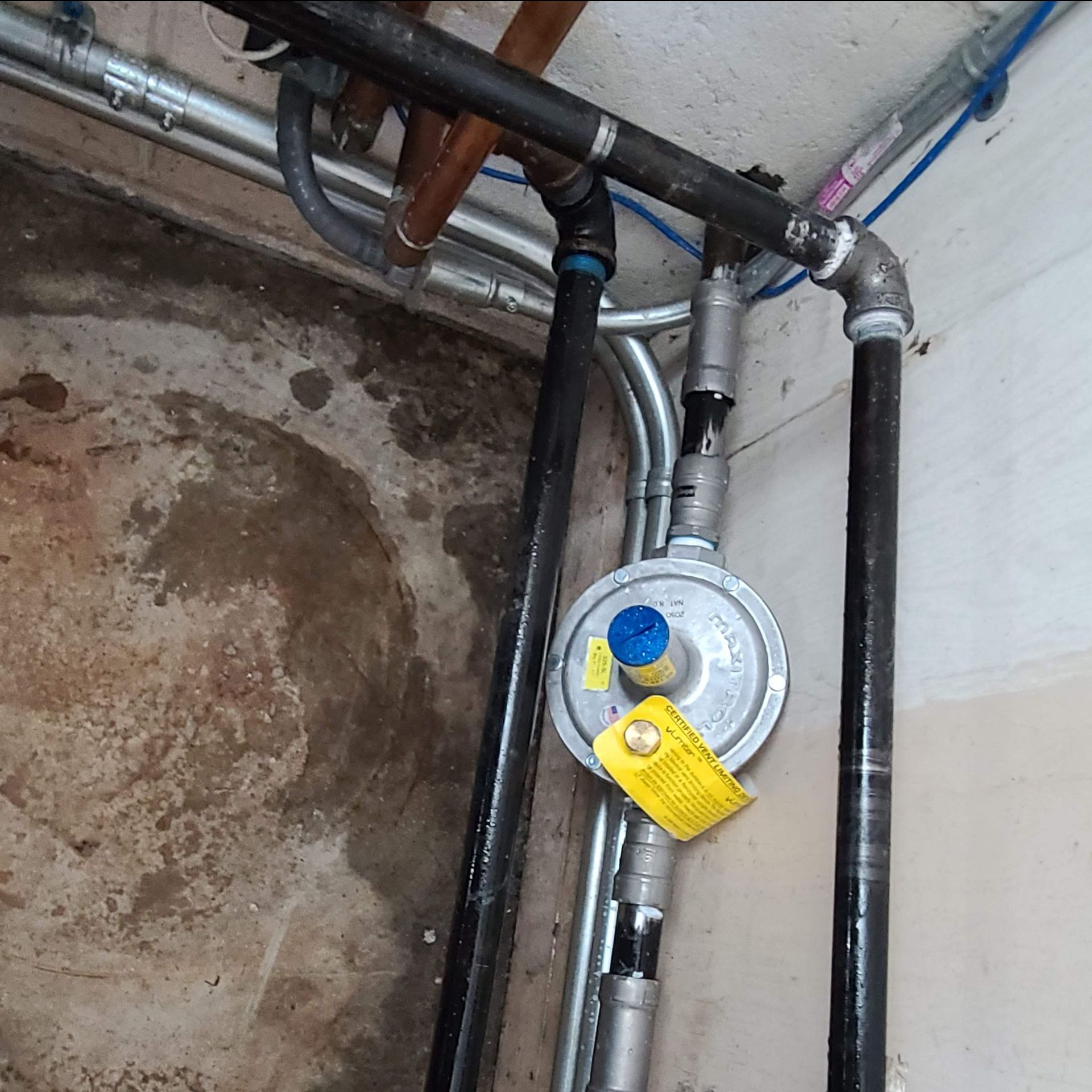 Gas regulator and piping in a basement, with a yellow tag attached to the regulator.