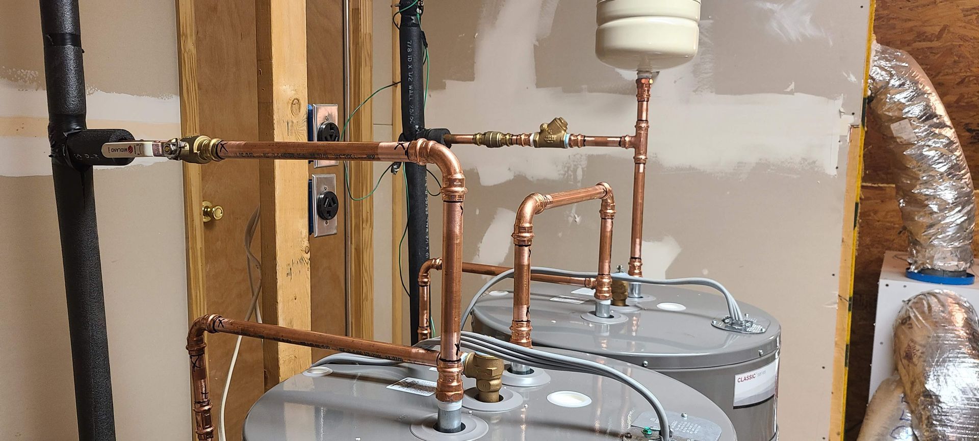 Copper pipes connected to two water heaters, along a wooden wall.