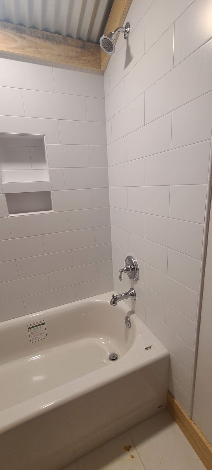 A white bathtub with a chrome faucet and showerhead in a bathroom with white tiled walls.