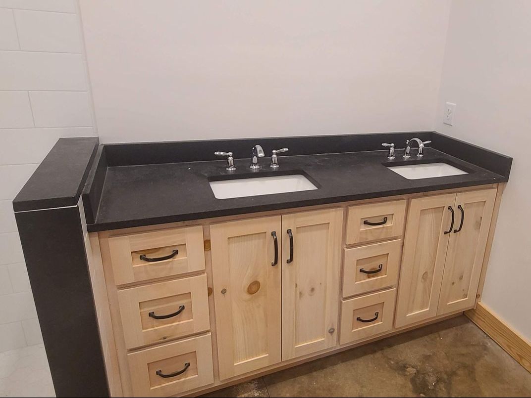 A bathroom vanity with a black countertop and two sinks, sitting on a light wood cabinet.
