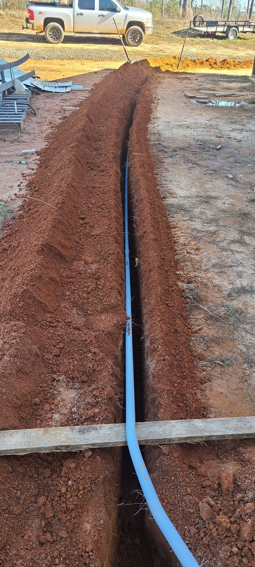 A trench with a blue pipe running through it, with a truck in the background.