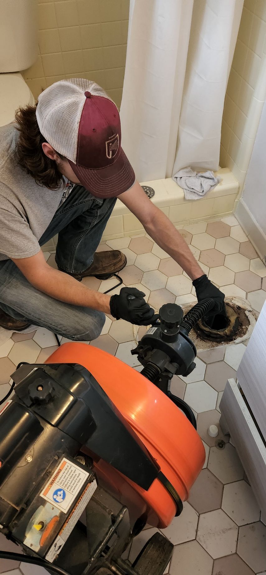 Person in a bathroom fixing a toilet, next to a cable drain cleaner.