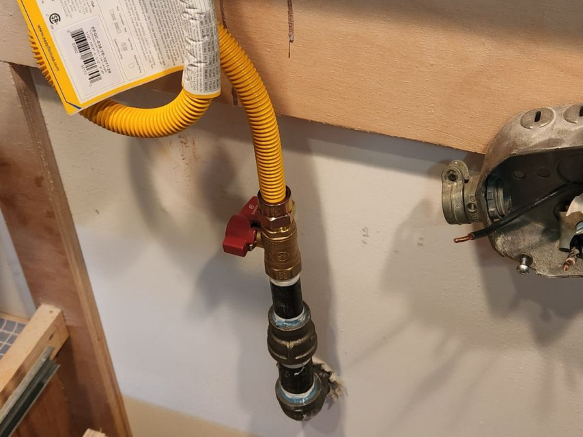 Yellow gas line and red valve connected to a black pipe on a wall.