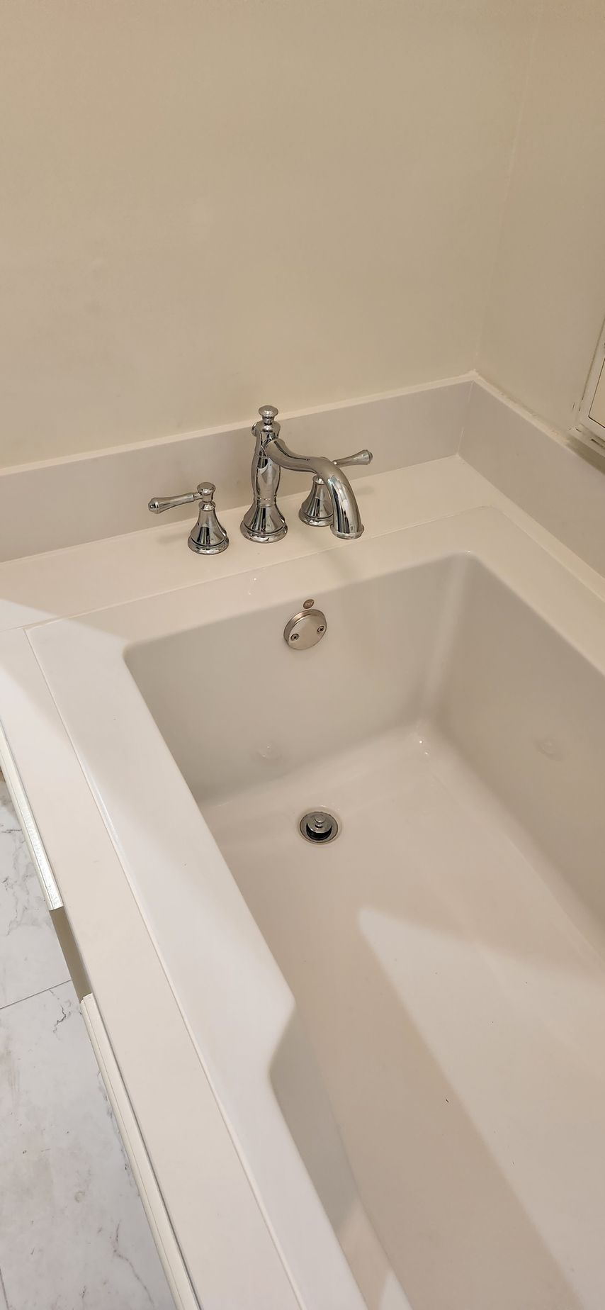 A white bathtub with silver fixtures. The tub is empty, and in a bright bathroom.