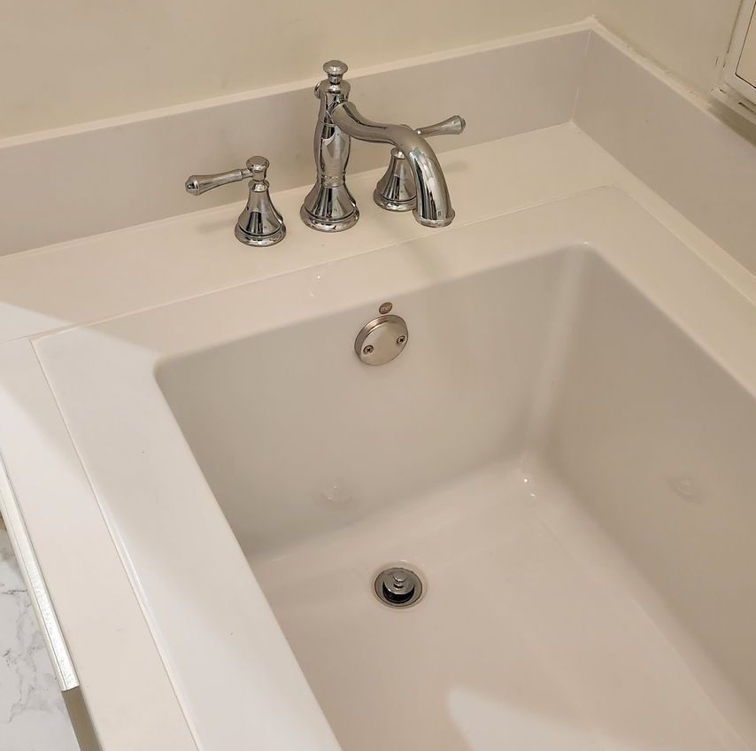 White bathtub with chrome faucet and drain, built into a white countertop.