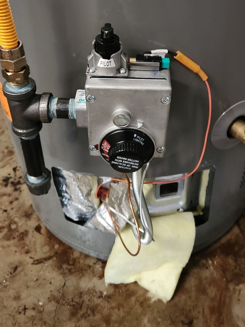A close-up of a gas water heater's control panel and gas line. The panel has a black temperature dial.