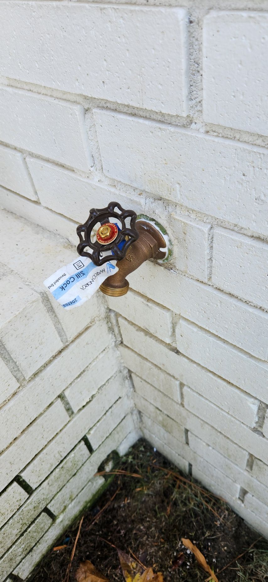 A water spigot on a brick wall with a tag hanging on the spout.