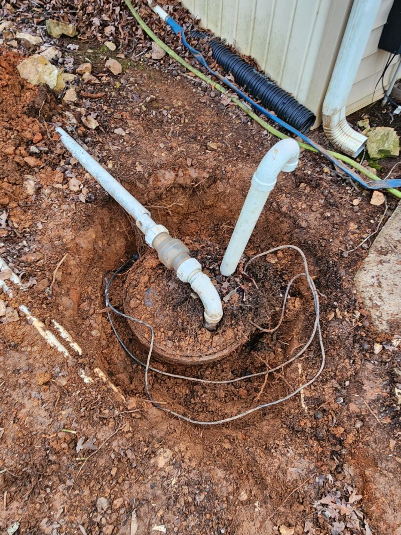 Open well with pipes and wires in a muddy yard.