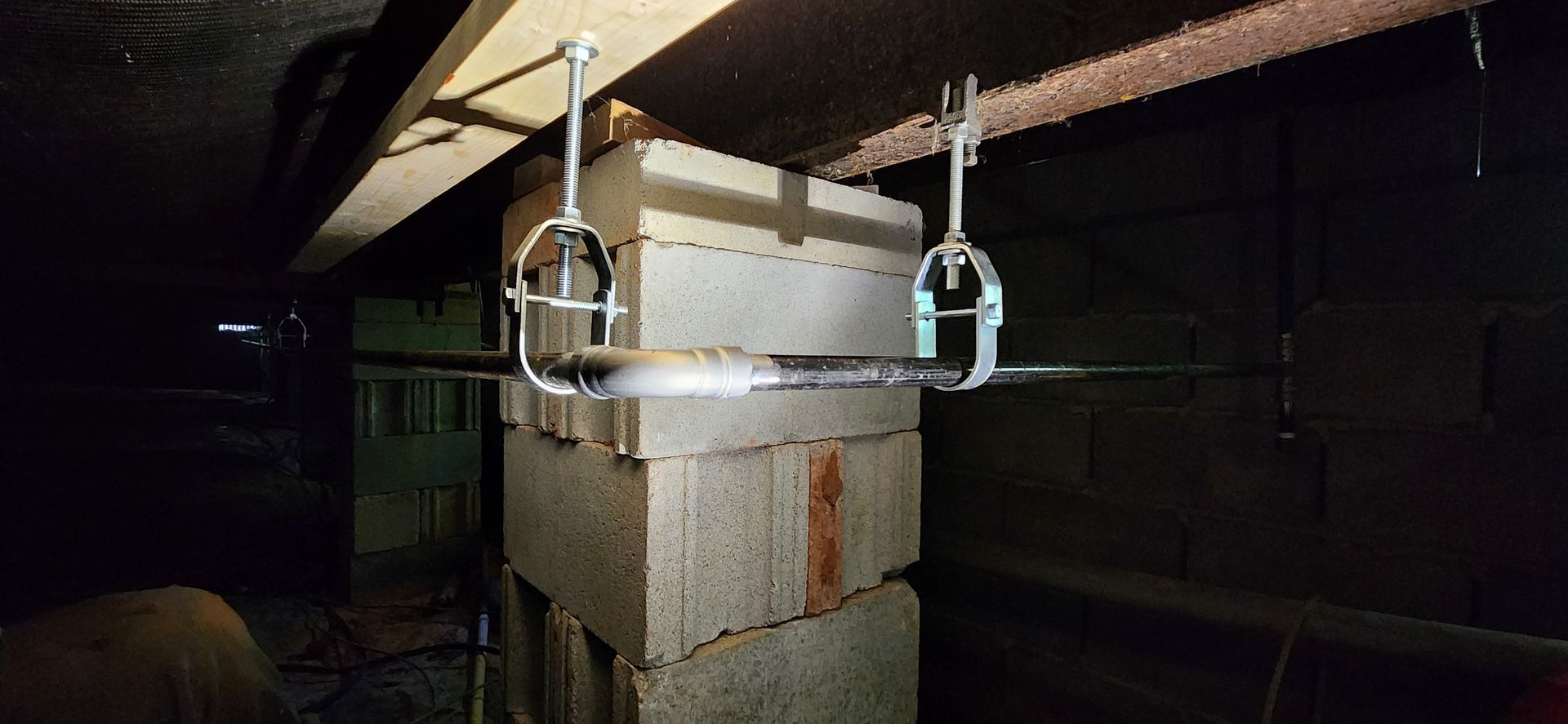 Cinder blocks supporting a beam, held by metal clamps. Dark, enclosed space.